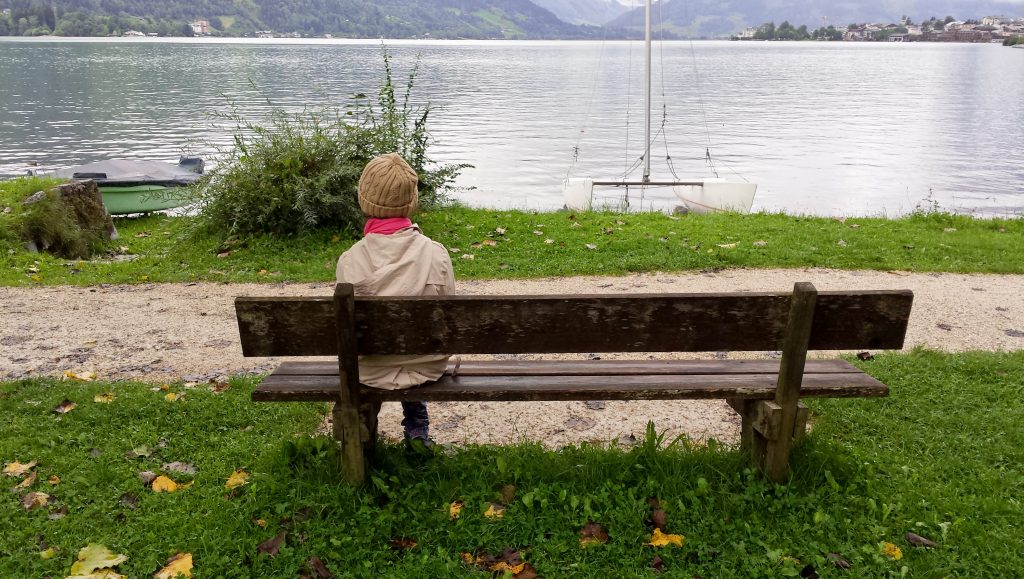 Warmly dressed person sitting alone on a bench, watching the harbor.