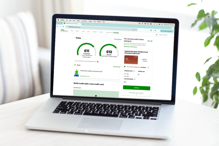 An image of a MacBook laptop on a white table or desk, a plant is seen peeking on the right side of the image. The computer screen shows a Credit Karma account's dashboard.