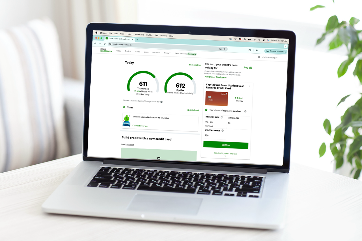 An image of a MacBook laptop on a white table or desk, a plant is seen peeking on the right side of the image. The computer screen shows a Credit Karma account's dashboard. 