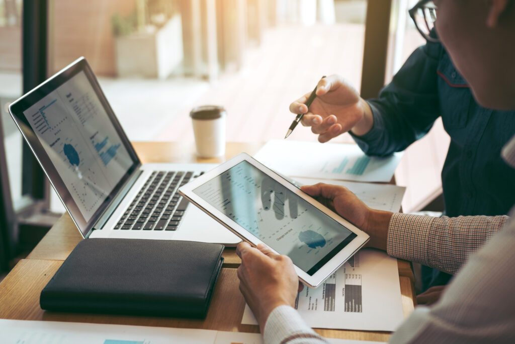 Two professionals reviewing financial data on a tablet and laptop during a meeting at a modern office desk.