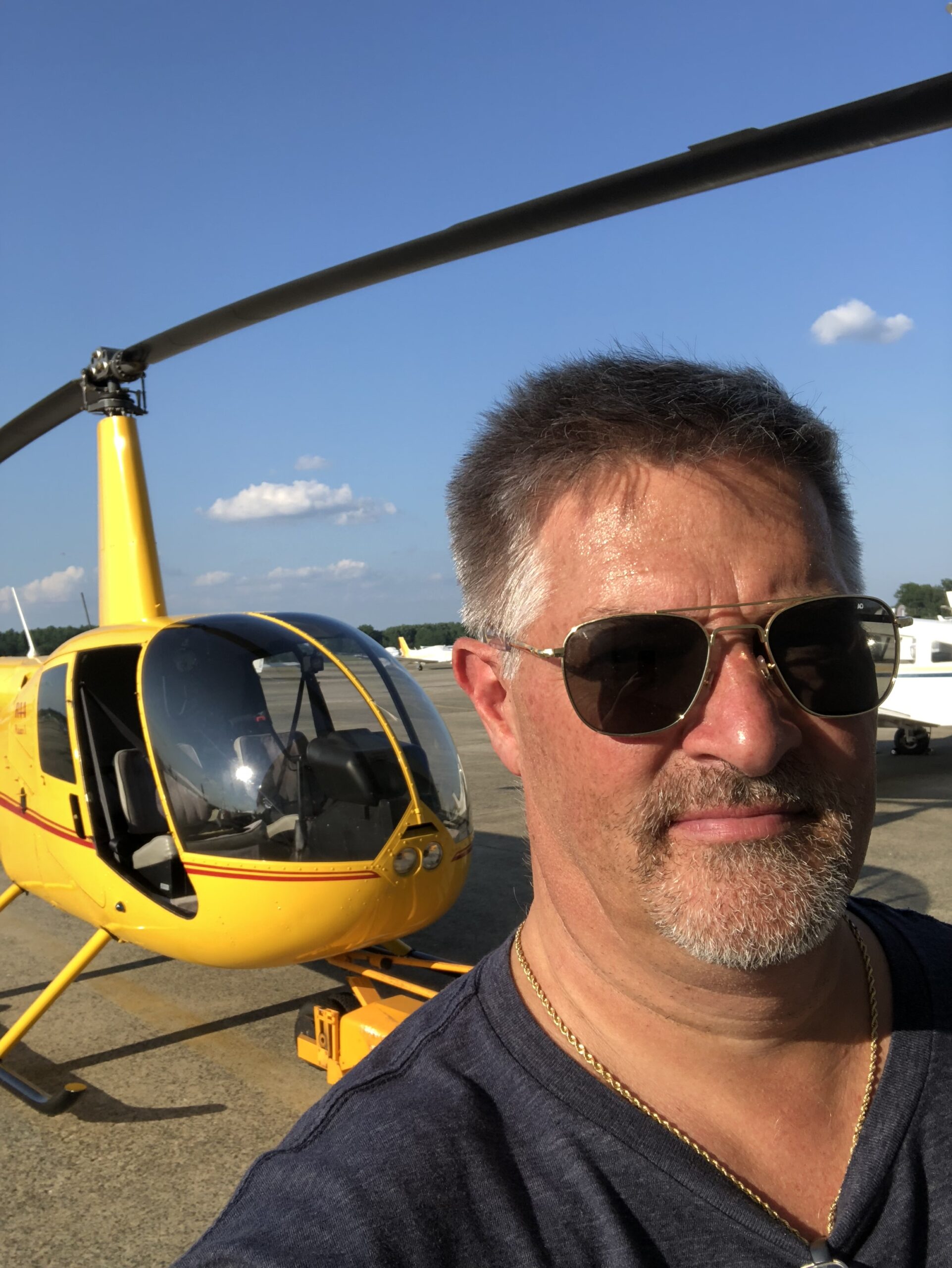 Eric C. Jansen wearing sunglasses pictured in front of a yellow helicopter on the tarmac